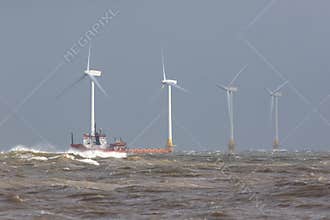Ship on rough sea horizon by offshore wind farm turbines