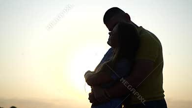 Guy hugs his girlfriend from behind against sunset in summer, close-up in slow motion. Romantic date of young happy