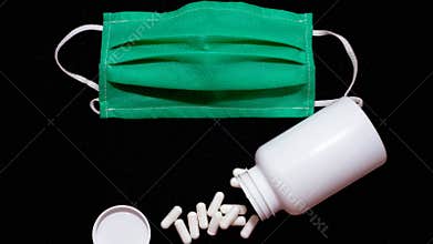 Medical mask on a black background,a protective mask against viruses an antiviral agent, capsules,spilled tablets,a white medical