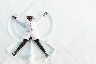 Black girl lies on white forest glade and makes snow angles