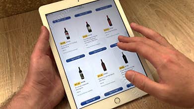 A man chooses wine and other types of alcohol in an online store using a tablet. The choice of goods in the online store