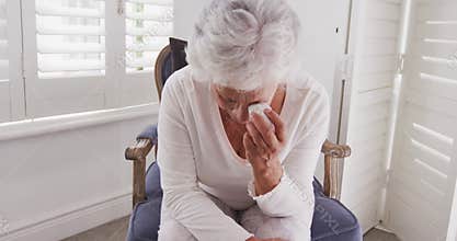 Senior African American woman crying and weeping tears with tissue at home