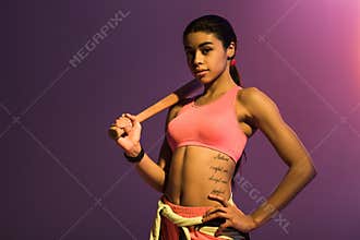 African american girl with baseball bat posing at camera with hand on hip on purple background