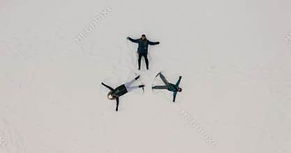 Aerial top view of happy three people having fun during winter vacation playing with snow doing angel during Christmas