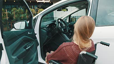 Young disabled woman getting out of the car in the wheelchair