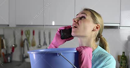 apartment flooded by upstairs - woman calling repair service while water leaking from ceiling in bucket