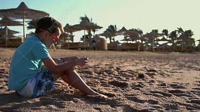 Cute teenager playing mobile phone at seashore. Young man enjoying sea at beach.