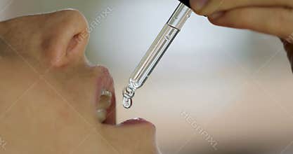 Woman taking vitamin or dietary supplement drops in mouth from dropper. herbal alternative medicine
