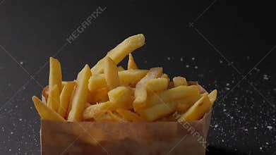 Package, bag with fries, salt is poured on top. Black background. Slow motion.