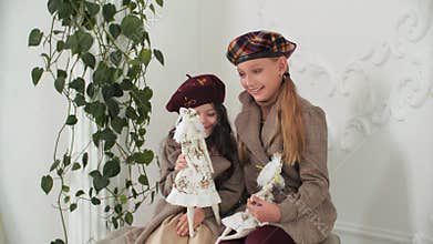 Adorable stylish girls in coats and berets posing with elegant vintage dolls