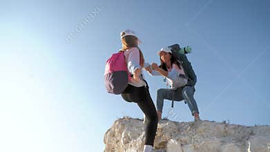 Girl helps her friend climb up the last section of mountain. Tourists with backpacks help each other, silhouette with