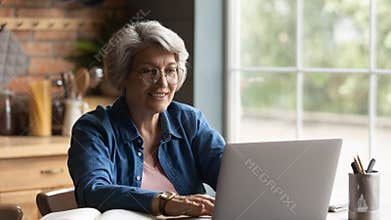 Elderly 60s woman look at laptop screen working at home