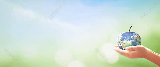 Conceptual Apple Shaped Planet Earth in Human Hands over Wide Panoramic Nature Bokeh Background