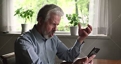 Old man holding smartphone experiences difficulties with modern gadget usage