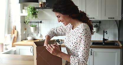 Woman opens parcel looks inside feels satisfied with ordered items