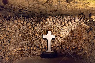 Stack of skulls and bones with a white cross in the catacombs of Paris France