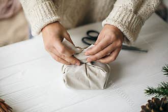 Woman in cozy sweater preparing plastic free christmas present, zero waste holidays. Female hands wrapping christmas gift in linen