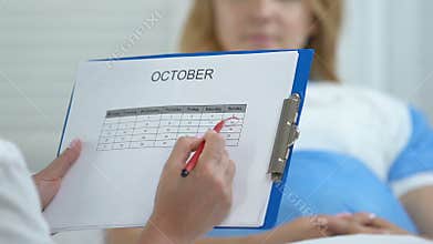 Doctor marking date in calendar talking female patient, breast cancer awareness