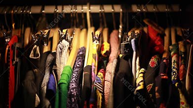 Plenty of various colorful female clothes hanging in the wardrobe in the dark, then little closet light turns on.