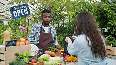 Friendly African American man selling bread and cabbage to customer in market