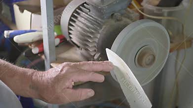Adult specialist sharpening steel knife on wheel lathe. Man grinding on abrasive cutting and knife-sharpening stones