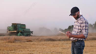Farmer uses a digital tablet in the background of a working combine
