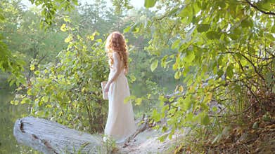Side view of a young elegant woman in light white dress standing in the autumn forest with a straw basket. Fairytale