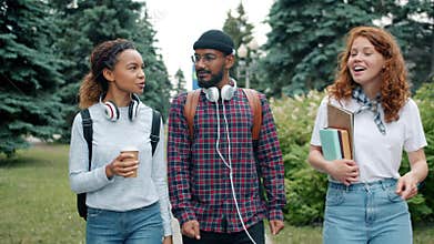Group of mates walking outdoors on campus with books and coffee chatting