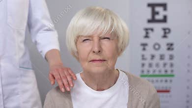 Optician comforting elderly woman squeezing eyes during sight examination, care