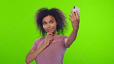 Glad black woman smiles broadly, takes selfie portrait on white cell phone