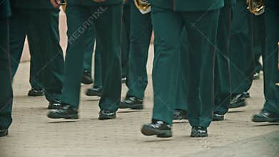 A wind instrument parade - people in green costumes walking on the street holding musical instruments - military musical
