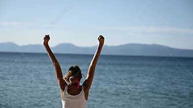Woman by the sea enjoying life as she lifts her arms high up in celebration