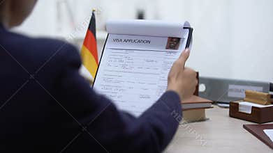 Embassy employee approving visa application, German flag on table, authority