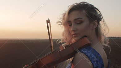Silhouette of a young woman figure in the sunrays playing the violin, girl relaxing and moving bow along the strings of a musical