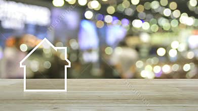 House flat icon with copy space on wooden table over blur light and shadow of shopping mall, Business real estate concept