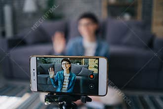 Joyful girl recording video with smartphone camera talking waving hand at home