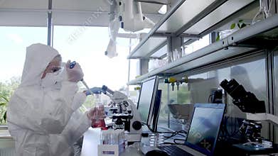 Scientists in protection suits and masks working in research lab using laboratory equipment: microscopes, test tubes