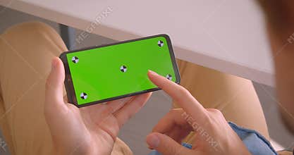 Closeup back view portrait of male scrolling on phone with green screen indoors