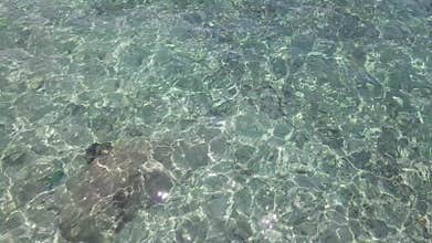 Sea Surface Ripple at Sunlight with Transparent Clear Water and Visible Sandy Bottom with Underwater Rocks. Aerial Top