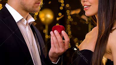 Male holding gift box with jewelry, presenting girlfriend for birthday at party