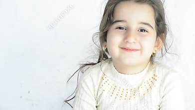 Close up portrait of a happy little girl looking directly to camera in front of white wall