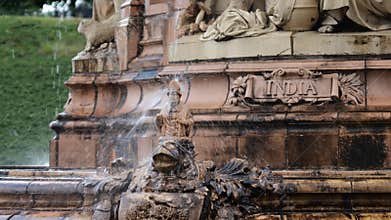 Water falling on a small figure of bishop at Doultoun Fountain in Glasgow Green Park with India sign in the background