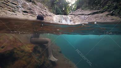 Pretty young woman sitting at pristine waterfall stream in the forest.