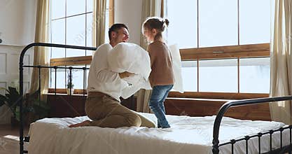 Carefree small daughter and dad playing pillows fight in bed
