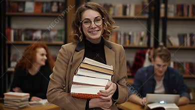 Portrait of attractive european girl student holding books in high school library smiling looking at camera. Education