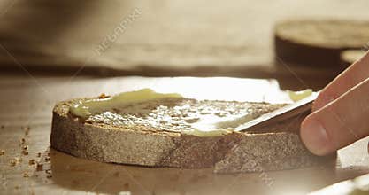Spreading Butter on Fresh Artisan Rye Bread Slice with a Knife Close up of a Palm on a Wooden Table with Sunshine and Sun Flares S