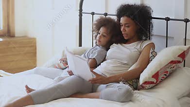 Pleasant biracial woman reading book to daughter.