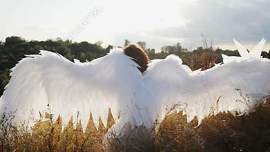 White angel sitting on dry grass on a hill