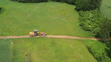 Road leveling motor grader on bad farmland road at work, aerial
