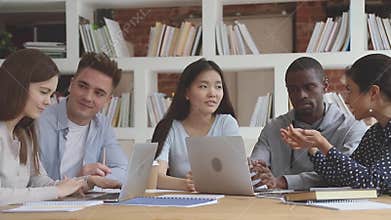 Diverse people sitting at table, studying in groups on computers.